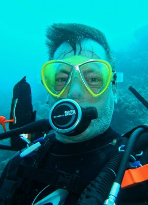 Close-up of a scuba diver with yellow goggles underwater in Indonesia's diverse marine ecosystem.
