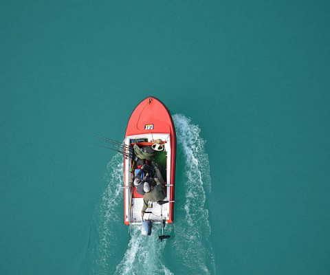 Top view of a red motorboat with fishermen navigating open turquoise waters.