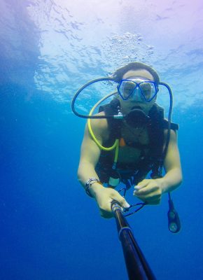 A scuba diver explores the vibrant underwater world in Thailand, capturing the moment with a monopod.